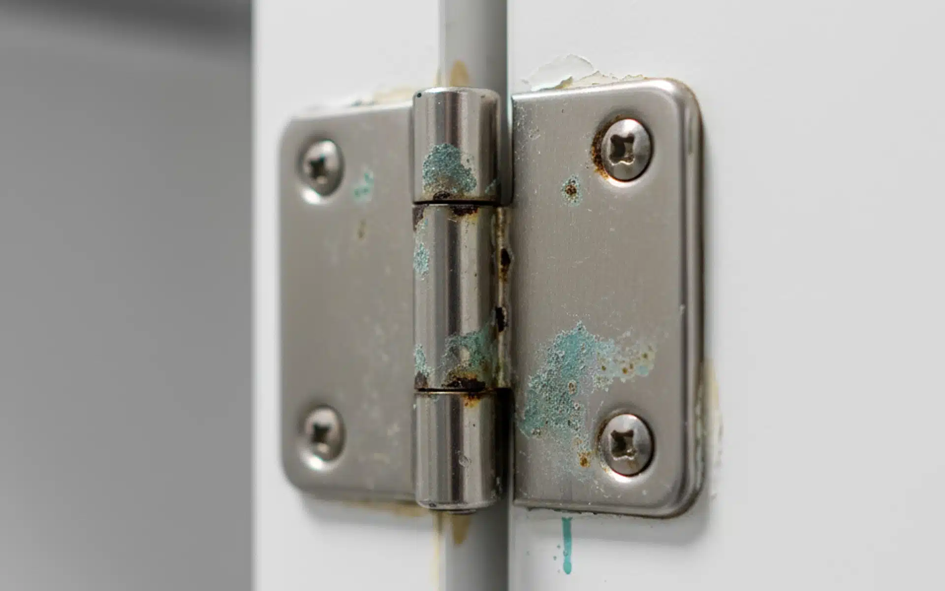 A close-up of a rusty, corroding metal door hinge with peeling paint, highlighting the need for durable hardware replacement.